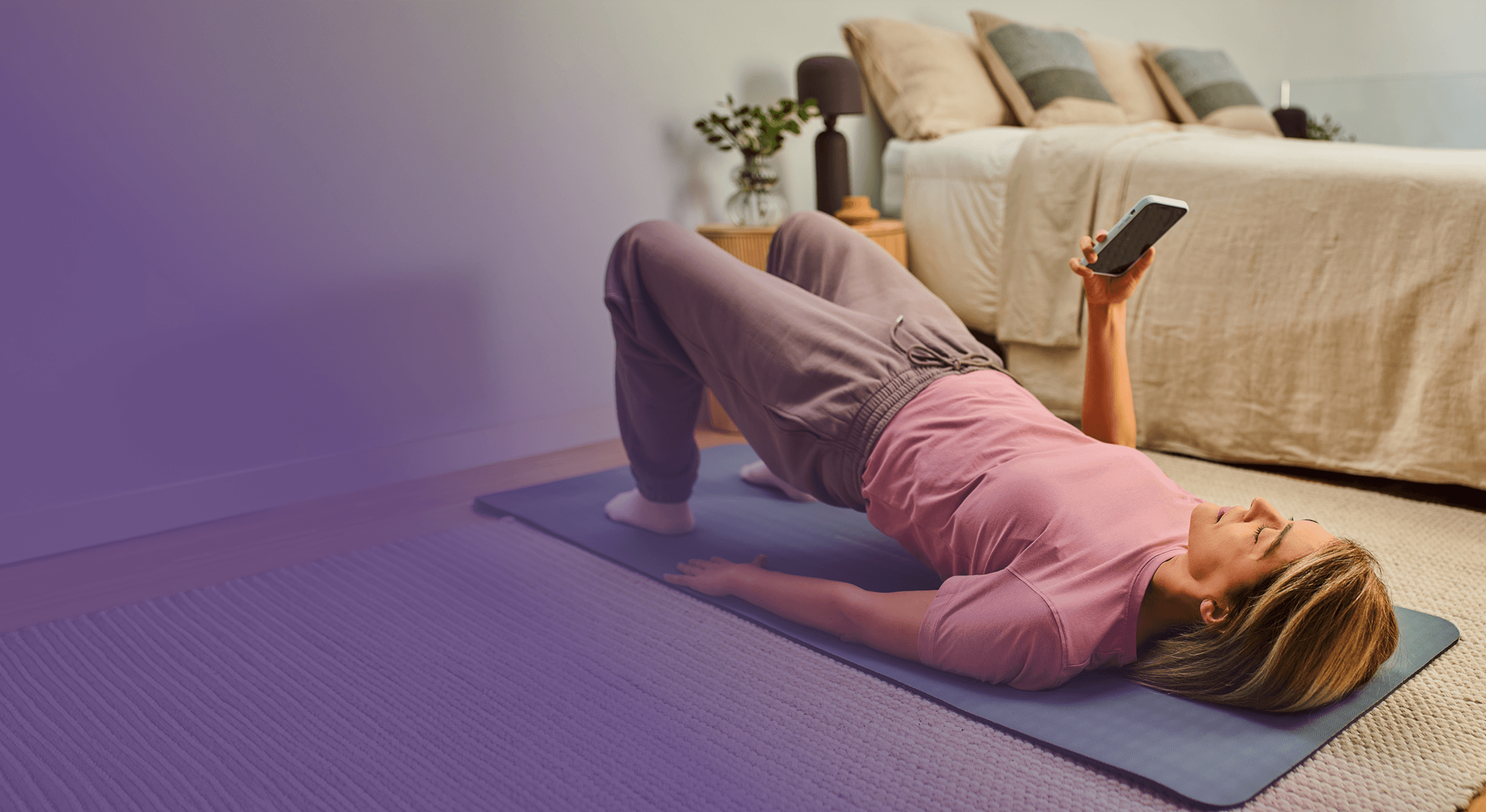 A person on a yoga mat performing a glute bridge exercise while looking at their phone.